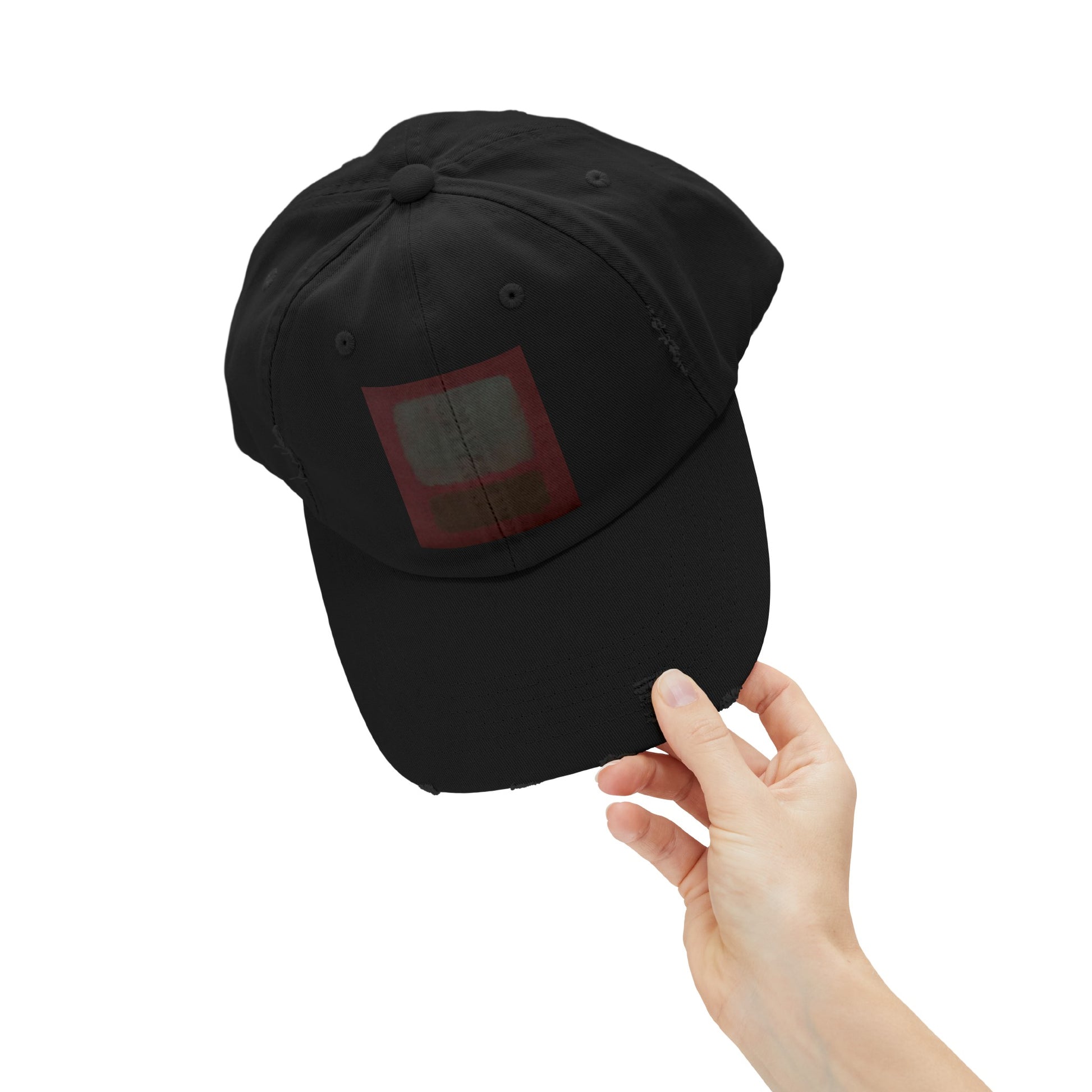 a hand holding a black hat with a red square on it